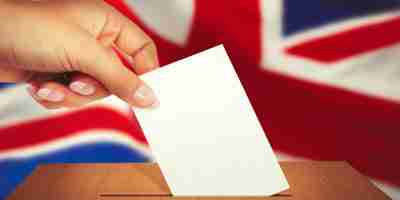 Hand putting voting card in ballot box in front of the United Kingdom flag. What does a Labour victory mean for corporate immigration?