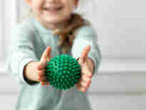 A young toddler holding green rubber physio ball in the foreground. Multi Trauma injury claims solicitors