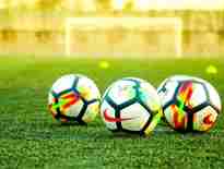 three footballs on the ground in front of a football pitch. News 07 June 2024 'Football’s coming home?'—Exploring the legal implications of football-related injuries in the lead up to Euro 2024