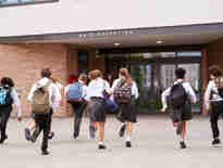 Eight school children running towards a school building. Disputes with independent and state funded schools