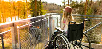 Young girl in a wheelchair on a balcony overlooking a river and tall trees. Spinal cord injury compensation claim solicitors