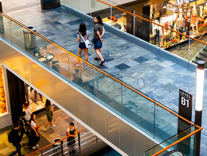 A shopping centre with two women walking over a tiled floor bridge above additional exposed floors and shops below